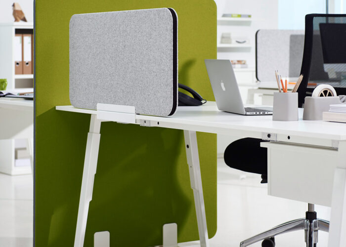 Ein moderner Büroarbeitsplatz mit weißem Schreibtisch, grünem Sichtschutz, Laptop, Büromaterial und einem schwarzen Stuhl. Der Bereich ist durch große Fenster mit natürlichem Licht hell erleuchtet.