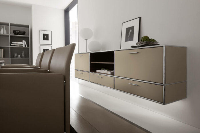 Minimalistischer, moderner Raum mit beigen Schwebeschränken, einer Reihe brauner Stühle, Wandkunst, Regalen mit Dekoration und einem großen Fenster, das natürliches Licht hereinlässt.